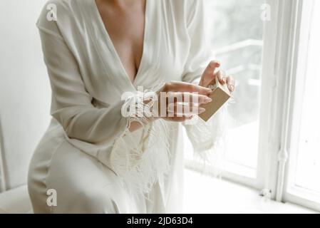 Der Morgen der Braut. Die Braut in ihrer Robe sitzt am Fenster und zieht ihre Hochzeitszubehör an Stockfoto