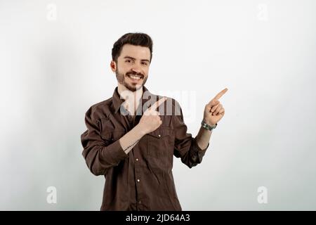 Fröhlicher Casual-Mann in legerer Kleidung, der isoliert auf weißem Hintergrund lachend posiert und mit zwei Händen und Fingern auf die Kamera zeigt Stockfoto