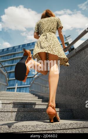 Rückansicht einer Frau, die auf Treppen geht und die Sohle ihrer Sandalen zeigt Stockfoto