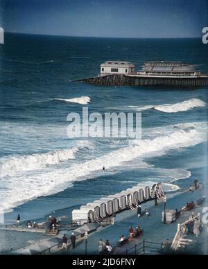 Raue Meere an der Küste von Norfolk in Cromer, England, mit seinen Strandhütten und dem Pier im Hintergrund. Kolorierte Version von : 10167326 Datum: Anfang 1930s Stockfoto