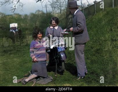 Zwei junge Motorradfahrerinnen, die anscheinend einen Tropfen Getränk von einem Mann mit einer Flasche, nicht alkoholisch, annehmen, hoffen wir. Kolorierte Version von : 10168273 Datum: Anfang 1930s Stockfoto