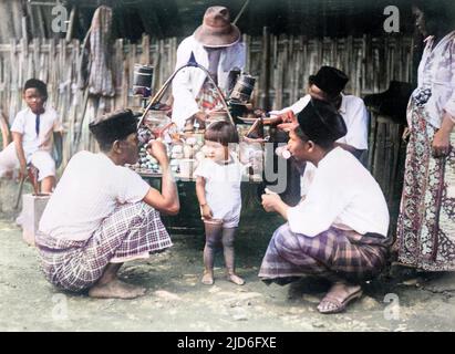 Zwei Männer mit Sarongs hocken sich herunter, um mit einem kleinen Jungen auf einem Basar in Java, Indonesien, zu plaudern. Kolorierte Version von : 10168474 Datum: Anfang 1930s Stockfoto