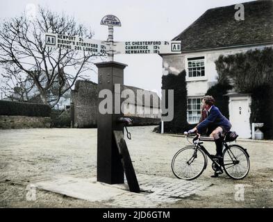 Das alte Zentrum des Dorflebens ist die „Village Pump“ in Littlebury, Essex, England. Diese Pumpe ist immer noch im Einsatz und wird von einem jungen Mann auf dem Fahrrad bewundert! Kolorierte Version von : 10185331 Datum: 1940s Stockfoto