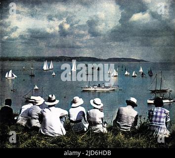 Eine Gruppe von Urlaubern, die die Brixham Regatta von einem Aussichtspunkt auf einer Klippe des West Country aus beobachten, 1936. Eine Reihe von Fischtrawlern mit dunklen Segeln teilen sich das Wasser mit den weißen Segeln von Rennyachten. Kolorierte Version von: 10218027 Datum: 1936 Stockfoto