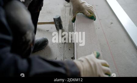 Der Meister legt eine Mauer aus Blöcken. Der Bauherr baut auf der Baustelle eines Wohngebäudes mit eigenen Betonwänden aus Zementblöcken Stockfoto