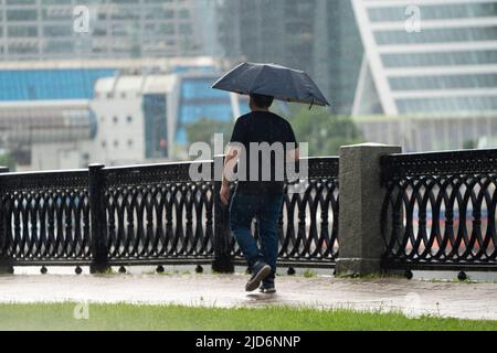 Moskau, Russland - 17. Juni 2022: Regen in Moskau. Ein Mann mit einem Regenschirm läuft am Schewtschenko-Damm in Moskau entlang. Hochwertige Fotos Stockfoto