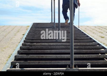 Die Beine eines älteren Mannes mit Stock. Er steigt eine öffentliche Treppe auf einen Deich. Stockfoto