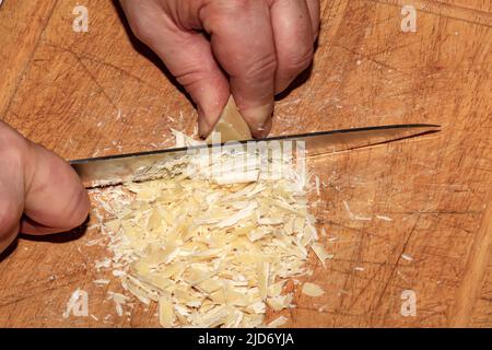 Die Hände des Kochers mahlen Kakaobutter mit einem Messer auf einem hölzernen Küchenbrett, um Schokolade zu machen. Stockfoto