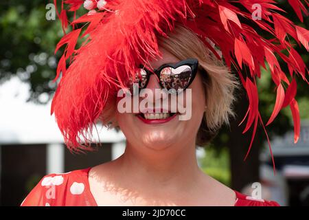 Ascot, Bergen, Großbritannien. 18.. Juni 2022. Milliner Sally Harper trägt einen ihrer roten Kopfbedeckungen. Racegoers, die in Royal Ascot ankamen, sahen für den letzten Tag von Royal Ascot sehr glamourös aus. Nach einer Woche strahlenden Sonnenlichtes gab es heute Morgen ein paar Regenstellen, so dass die Regenschirme eine Weile in Aktion waren. Quelle: Maureen McLean/Alamy Live News Stockfoto