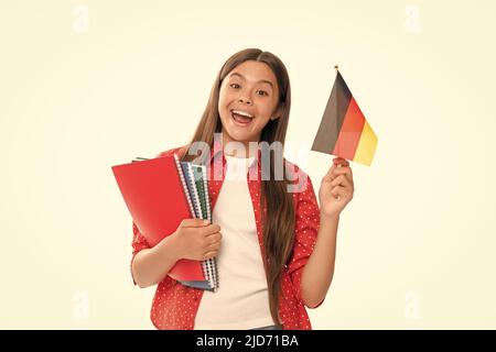 Überraschendes Kind hält deutsche Flagge und Schulkopiebuch für das Studium isoliert auf weißer, deutscher Sprache Stockfoto