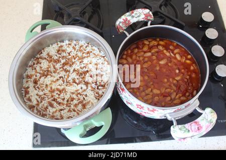 Pinto- oder Nierenbohnen und Reispilaf im Topf auf dem Herd. Nahaufnahme und Draufsicht auf gekochte Pinto-Bohnen und Reispilaf. Stockfoto