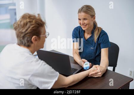 Der Arzt misst die Temperatur des Patienten mit einem berührungslosen Thermometer während eines Termins Stockfoto