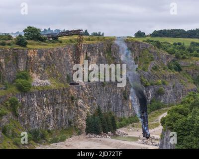 ***Video verfügbar*** Mission: Impossible 7 Lokomotivzug-Crashszene in Stoney Middleton, Derbyshire. Der nachgebaute Dampfzug der British Railway Britannia wird für die letzte Crashszene in Tom Cruise's neuestem Blockbuster-Film von der Klippe getrieben. Die Lokomotive fliegt in spektakulärem Stil durch die Luft, bevor sie in den Steinbruch darunter stürzt. Die Szene wurde von zwei Hubschraubern und vielen entfernten Kameras gefilmt. Tom Cruise kam kurz vor der letzten Absturzszene in seinem Personalhubschrauber an, er flog um den Film, bevor er auf den Feldern in der Nähe der Eisenbahnstrecke über dem Steinbruch landete. Der Dampfstoß tr Stockfoto