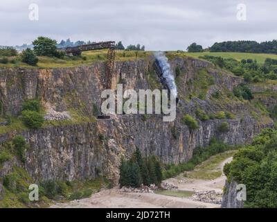 ***Video verfügbar*** Mission: Impossible 7 Lokomotivzug-Crashszene in Stoney Middleton, Derbyshire. Der nachgebaute Dampfzug der British Railway Britannia wird für die letzte Crashszene in Tom Cruise's neuestem Blockbuster-Film von der Klippe getrieben. Die Lokomotive fliegt in spektakulärem Stil durch die Luft, bevor sie in den Steinbruch darunter stürzt. Die Szene wurde von zwei Hubschraubern und vielen entfernten Kameras gefilmt. Tom Cruise kam kurz vor der letzten Absturzszene in seinem Personalhubschrauber an, er flog um den Film, bevor er auf den Feldern in der Nähe der Eisenbahnstrecke über dem Steinbruch landete. Der Dampfstoß tr Stockfoto