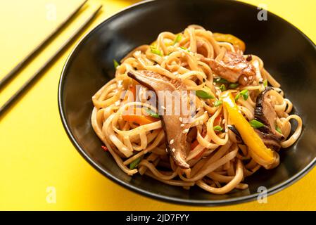 Ein traditionelles asiatisches Gericht. Chinesische udon-Nudeln auf einem schwarzen Teller auf gelbem Hintergrund Stockfoto