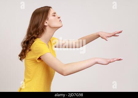 Blindheit, verloren in der Dunkelheit. Profil eines verärgerten Teenagers in gelbem T-Shirt, das mit geschlossenen Augen steht und frustriert und desorientiert ist. Innenaufnahme des Studios isoliert auf grauem Hintergrund. Stockfoto