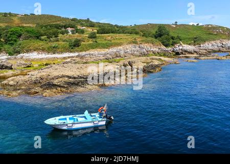 Kleines Motorboot mit großen Felsen und transparentem Wasser, das am Ufer geparkt ist. Stockfoto