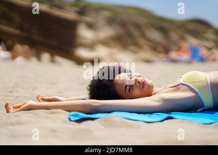 Zufriedene junge afroamerikanische Frau, die am Sandstrand liegt und vor der Kamera zwinkern kann Stockfoto