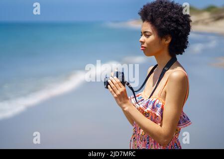 Schwarze Frau mit Kamera am Strand Stockfoto