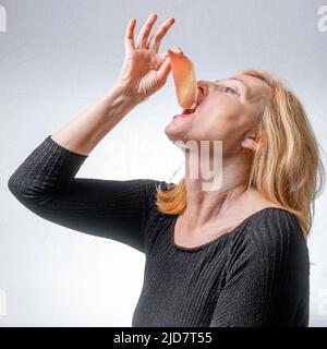Eine blonde Frau hält ein Stück italienischen Parmaschinken in der Hand neben ihren Mund, als sie es gerade essen will Stockfoto