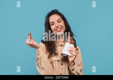 Zufriedene glücklich tausendjährige kaukasische weibliche Brünette Student in casual essen Schokolade bar Stockfoto