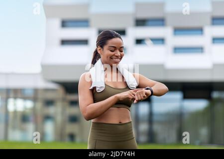 Porträt einer glücklichen jungen schwarzen Frau, die im Freien Smartwatch oder Fitnesstracker überprüft Stockfoto