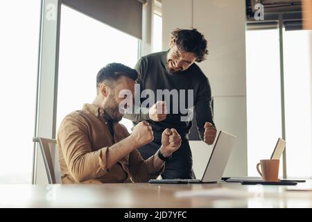 Aufgeregte männliche Kollegen feiern Erfolge, machen viel oder Einigkeit und geben IN der Nähe des Laptops im Büro JA Stockfoto