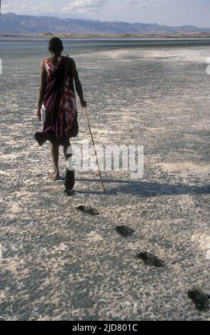 Ein Masai-Mann spaziert auf der ausgetrockneten Oberfläche des Lake Natron im Norden Tansanias. Stockfoto