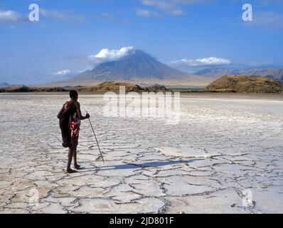 Ein Masai-Mann geht mit Ol Doinyo Lengai (der Berg Gottes - der heilige Berg des Stammes) im Hintergrund über die ausgetrocknete Oberfläche des Natron-Sees. Stockfoto