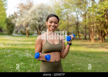 Fit junge schwarze Frau macht Übungen mit Hanteln im Stadtpark. Krafttraining Konzept Stockfoto