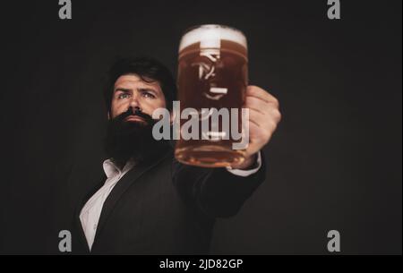 Schöner bärtiger Mann, der Bier trinkt. Porträt eines hübschen jungen Mannes, der ein Bier vom Fass probiert. Mann mit Bierkrug. Der Mann hält ein Glas Bier. Stockfoto