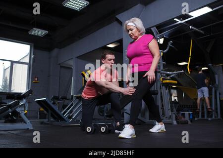 Ältere Frau, die unter persönlicher Traineraufsicht im Fitnessstudio Ausfallschritte macht Stockfoto