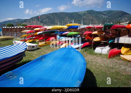 Viele bunte Plastikkajaks liegen auf Lagerregalen vor Bergen am Ufer des Mittelmeers. Kleine Boote im Lager Stockfoto