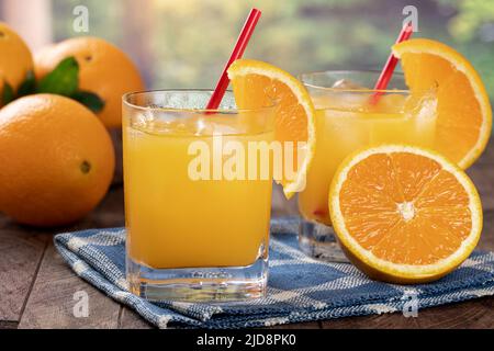 Ein Glas Orangensaft mit Eis und Orangenscheibe auf einem Holztisch mit ländlichem Sommerhintergrund Stockfoto