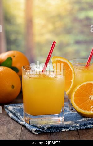 Ein Glas Orangensaft mit Eis und Orangenscheibe auf einem Holztisch mit ländlichem Sommerhintergrund Stockfoto