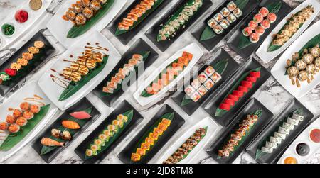 Banner mit verschiedenen Sets von Maki-Sushi-Rollen, Nigiri und Gunkan mit Tiger Shrimps, tomago, Lachs, Thunfisch, chuka-Salat, Thunfisch und Bambusblätter in einem Whi Stockfoto