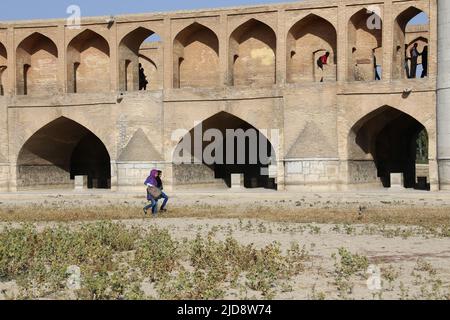 Allah-Verdi-Khan-Brücke in Isfahan, Iran. Auf personal heißt sie Si-o-se Pol. Die Brücke hat zwei Etagen und überspannt den Zayandeh Rud. Die Brücke hat 33 Bögen. Der Si-o-se Pol ist meist ausgetrocknet. Blick von der Flussseite auf die Brücke. Zwei Frauen queren den Fluss neben der Brücke. Stockfoto