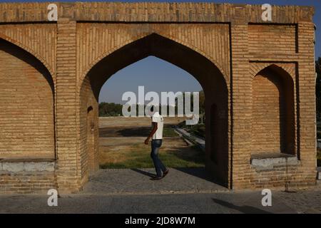 Allah-Verdi-Khan-Brücke in Isfahan, Iran. Auf personal heißt sie Si-o-se Pol. Die Brücke hat zwei Etagen und überspannt den Zayandeh Rud. Die Brücke hat 33 Bögen. Der Blick geht durch einen Steinbogen auf den Si-o-se Pol. Im Vordergrund ist eine Person zu sehen. Stockfoto