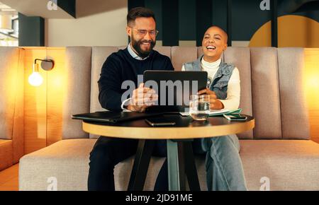 Unternehmer, die einen Videoanruf auf einem digitalen Tablet tätigen. Zwei junge Kreative lächeln fröhlich während einer Online-Konferenz mit ihren Mitarbeitern. Fröhlich Stockfoto