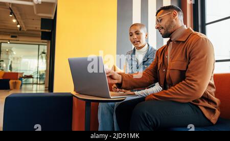 Moderne Geschäftsleute, die in einer Bürolobby eine wichtige Diskussion führen. Zwei junge Unternehmer, die einen Laptop in einem Co-Working-Space nutzen. Zwei junge Busin Stockfoto