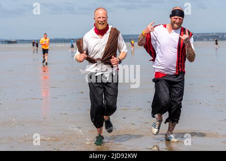 Thorpe Bay, Essex, Großbritannien. 19. Juni 2022. Ein Abschnitt des D-Day Mulberry Harbour aus dem Zweiten Weltkrieg wurde in der Themse-Mündung über eine Meile vor der Küste von Thorpe Bay in der Nähe von Southend on Sea nach Schwierigkeiten, als er 1944 unter Schlepptau lag, befahren und liegt seitdem dort. Es ist jetzt ein geplantes Denkmal und ist in zwei zerbrochen. Der riesige Phoenix Caisson ist bei Ebbe zu Fuß kurz erreichbar, obwohl viele von den RNLI gerettet werden mussten, wenn die Meerwasser zurückkehren. Der Wohltätigkeitslauf wurde sorgfältig geplant und überwacht, um die Läufer sicher zu halten, wobei der Erlös an die RNLI ging. Läufer im Piratenkostüd Stockfoto