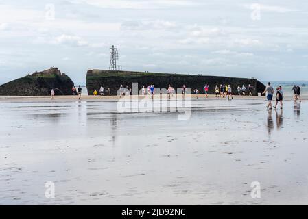 Thorpe Bay, Essex, Großbritannien. 19. Juni 2022. Ein Abschnitt des D-Day Mulberry Harbour aus dem Zweiten Weltkrieg wurde in der Themse-Mündung über eine Meile vor der Küste von Thorpe Bay in der Nähe von Southend on Sea nach Schwierigkeiten, als er 1944 unter Schlepptau lag, befahren und liegt seitdem dort. Es ist jetzt ein geplantes Denkmal und ist in zwei zerbrochen. Der riesige Phoenix Caisson ist bei Ebbe zu Fuß kurz erreichbar, obwohl viele von den RNLI gerettet werden mussten, wenn die Meerwasser zurückkehren. Der Wohltätigkeitslauf wurde sorgfältig geplant und überwacht, um die Läufer sicher zu halten, wobei der Erlös an die RNLI ging. Läufer erreichen den Mulberry Harbour Stockfoto