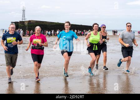 Thorpe Bay, Essex, Großbritannien. 19. Juni 2022. Ein Abschnitt des D-Day Mulberry Harbour aus dem Zweiten Weltkrieg wurde in der Themse-Mündung über eine Meile vor der Küste von Thorpe Bay in der Nähe von Southend on Sea nach Schwierigkeiten, als er 1944 unter Schlepptau lag, befahren und liegt seitdem dort. Es ist jetzt ein geplantes Denkmal und ist in zwei zerbrochen. Der riesige Phoenix Caisson ist bei Ebbe zu Fuß kurz erreichbar, obwohl viele von den RNLI gerettet werden mussten, wenn die Meerwasser zurückkehren. Der Wohltätigkeitslauf wurde sorgfältig geplant und überwacht, um die Läufer sicher zu halten, wobei der Erlös an die RNLI ging. Die Läufer kehren zurück zum Ufer Stockfoto