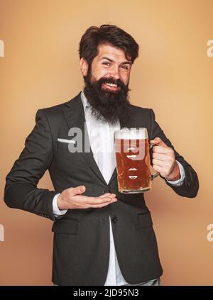 Bartmann trinkt Bier aus einem Bierkrug. Glücklicher lächelnder Mann mit Bier. Älterer Mann trinkt Bier mit Überraschungsgesicht. Stockfoto