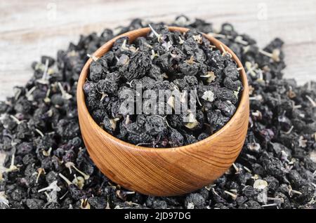 Die schwarzen Wolfbeeren oder schwarzen Goji-Beeren, in einer Holzschale auf dem Tisch. Stockfoto
