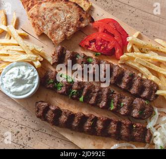 Kebab, Döner Souvlaki, gebratenes Fleisch, traditionelles Street Food. Ethno-Gericht, Pita-Brot, Tzatziki-Joghurt-Kartoffel und Zwiebel auf Holztisch, Draufsicht Stockfoto