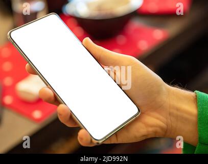 Leerer Bildschirm Smartphone auf einer männlichen rechten Hand, Nahaufnahme. Mann halten Handy mit leerem weißen Display, verwischen inneren Hintergrund zu Hause. Kopierbereich, Tem Stockfoto