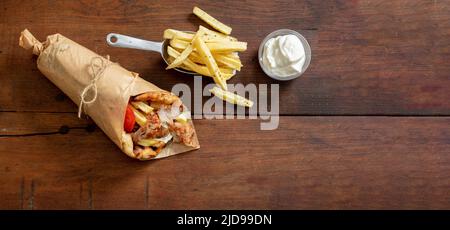 Gyro Pita Shawarma auf Holztisch. Griechische Lebensmittel, Fleisch in Scheiben, Kartoffeln, Tomaten und Zatziki, Papierverpackung, Draufsicht, Kopierbereich. Stockfoto