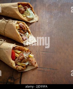 Shawarma Gyro Pita auf Holztisch. Griechische Lebensmittel, Fleisch in Scheiben, Kartoffeln, Tomaten und Zatziki, Papierverpackung, Nahaufnahme. Stockfoto