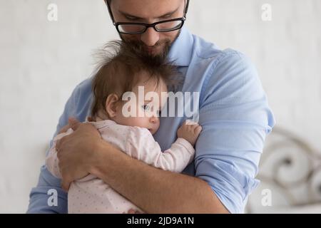 Fürsorglicher Vater hält sich an den Armen und beruhigt sein süßes Baby Stockfoto